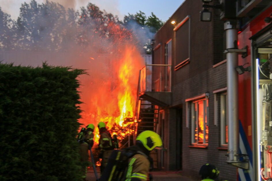 Heg en tuinhuis in brand, veel rook en vlammen te zien
